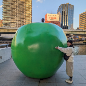 Flor Liu next to a large apple in a city